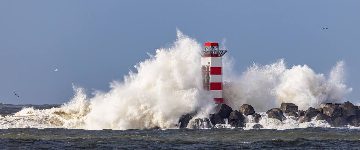 A lighthouse with red and white stripes, surrounded by crashing waves.
