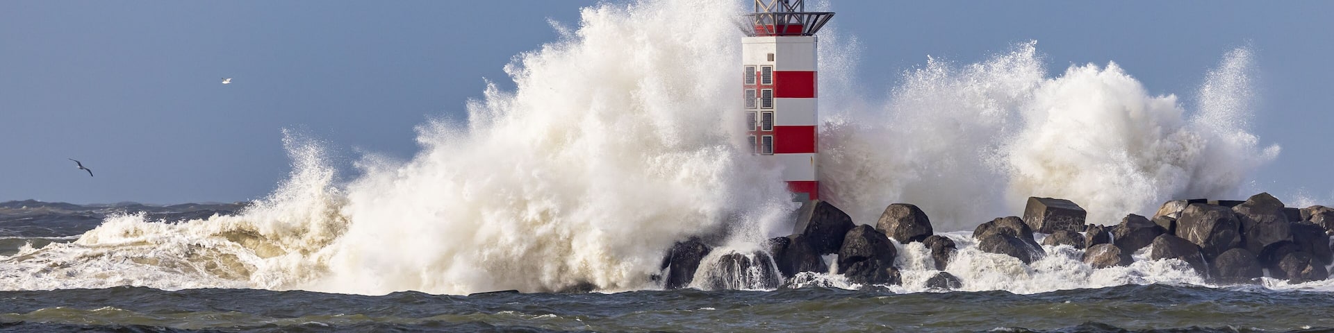 A lighthouse with red and white stripes, surrounded by crashing waves.