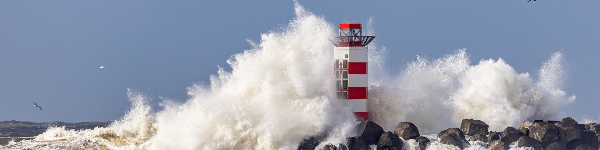 Um farol com listras vermelhas e brancas, cercado por ondas quebrando.