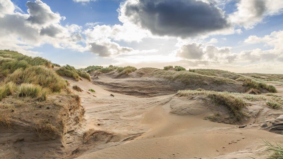 A sandy dune landscape with grassy vegetation and a partly cloudy sky.