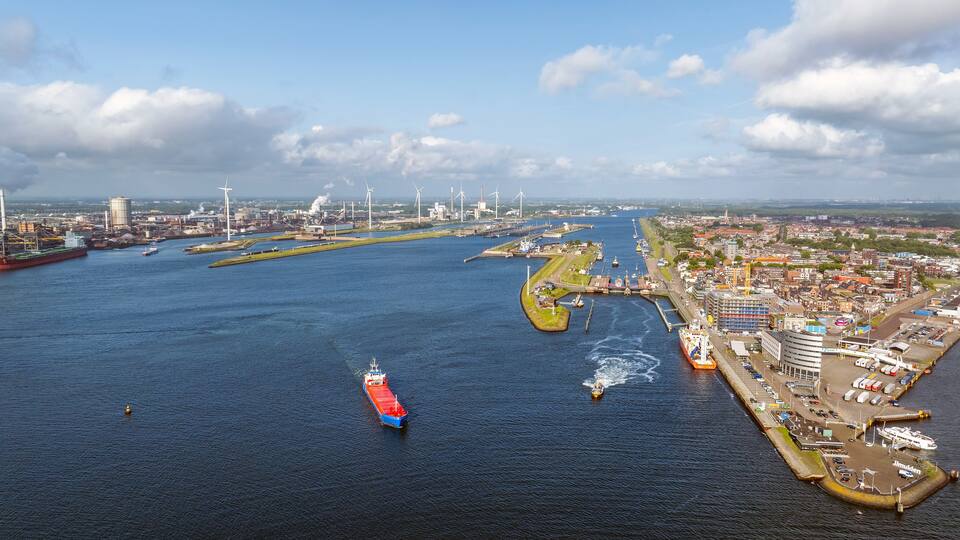 A coastal city with a harbor, wind turbines, and a large ship.