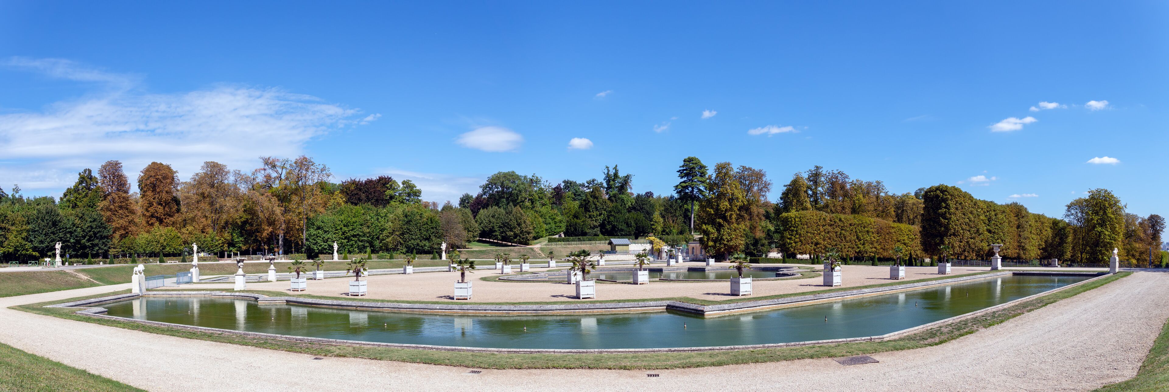 A formal garden with a central pond, statues, and neatly trimmed trees.