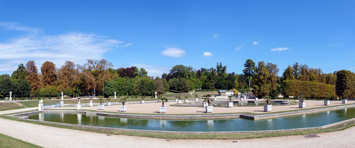 A formal garden with a central pond, statues, and neatly trimmed trees.