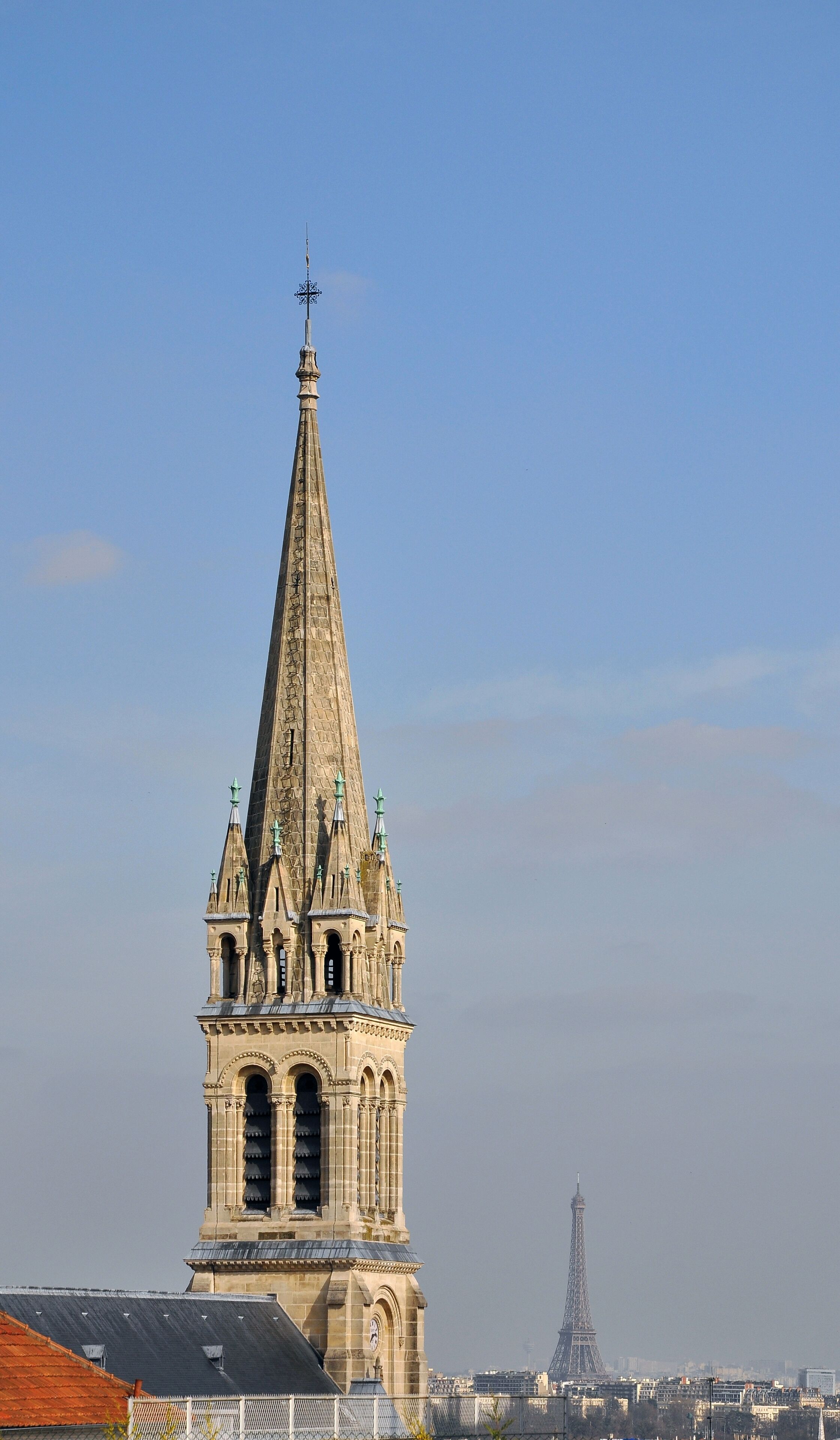 A church tower with a pointed spire and a cross at the top, set against a clear sky.