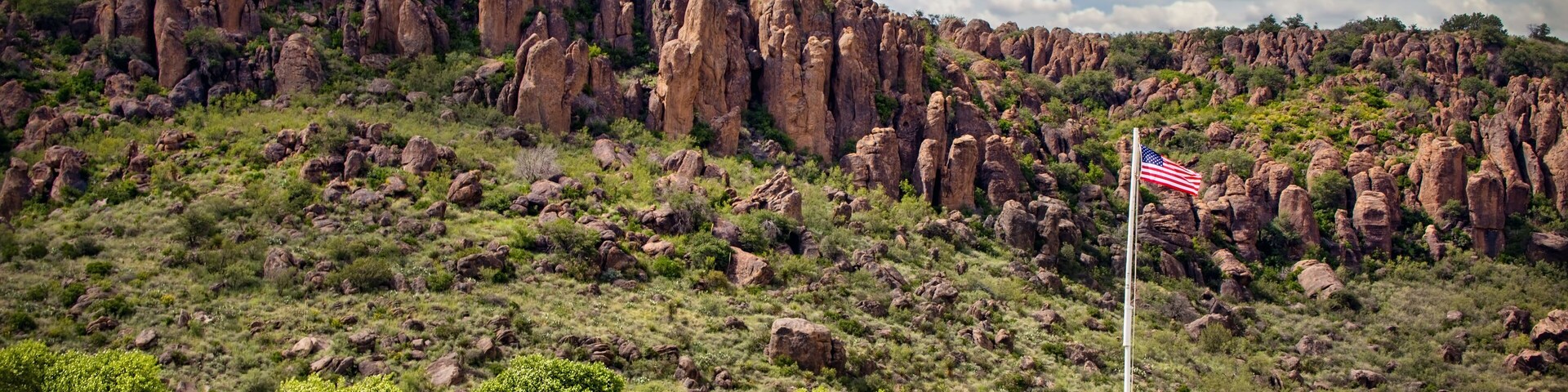 Ländliche Landschaft mit einer Häuserreihe, einem Fahnenmast mit der US-amerikanischen Flagge und einem felsigen Hügel im Hintergrund.