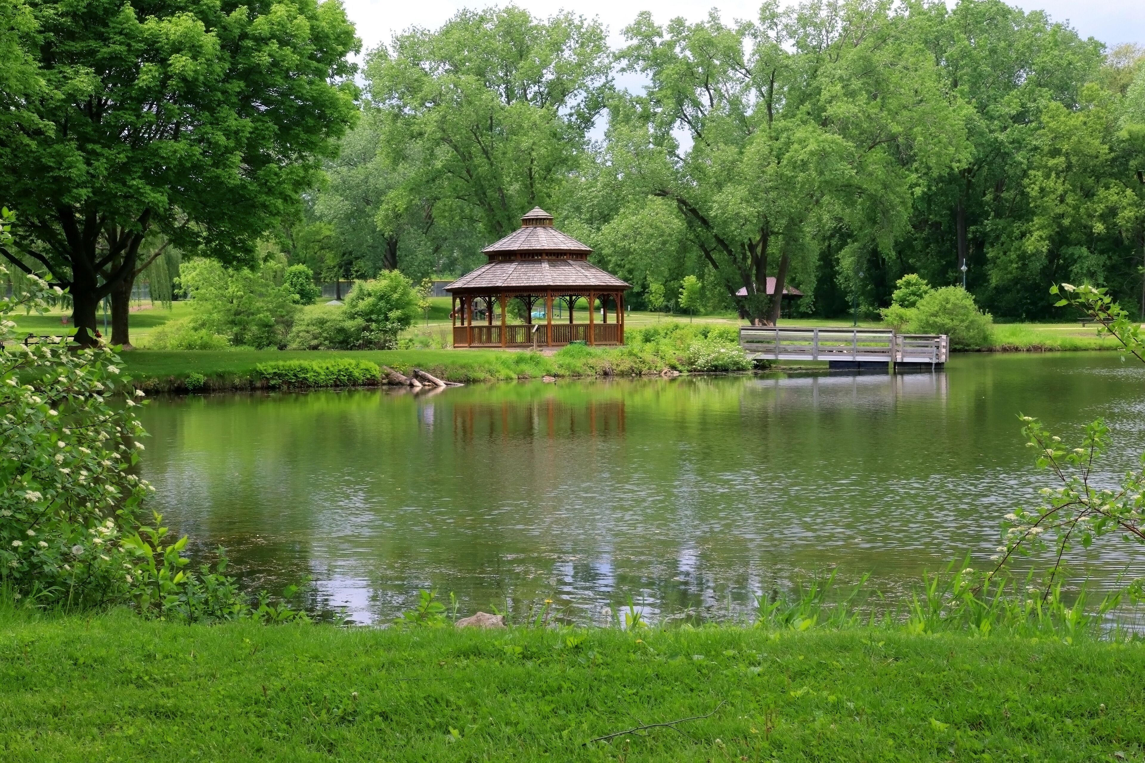 Midwest nature background with city park view. Beautiful late spring landscape with trees around the pond and wooden gazebo in a city park. Lakeview park, Middleton, Madison area, WI, USA.