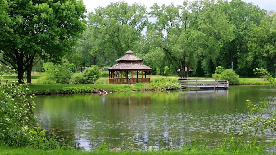 A gazebo by a pond surrounded by lush greenery and trees.