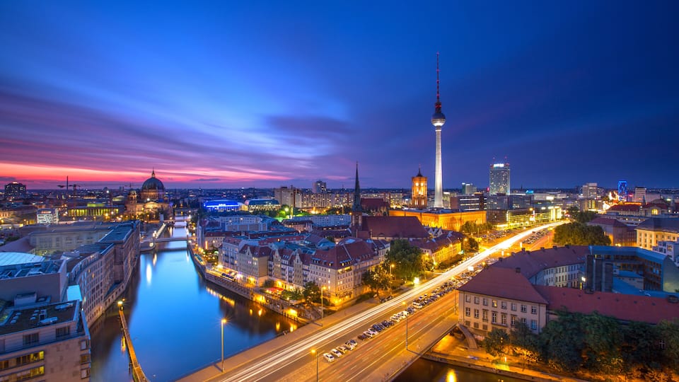 A cityscape at dusk with a prominent tower, a river, and illuminated buildings.