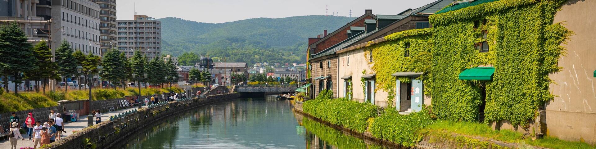 A calm canal with buildings on either side, including a house covered in ivy and a modern building with a dome.