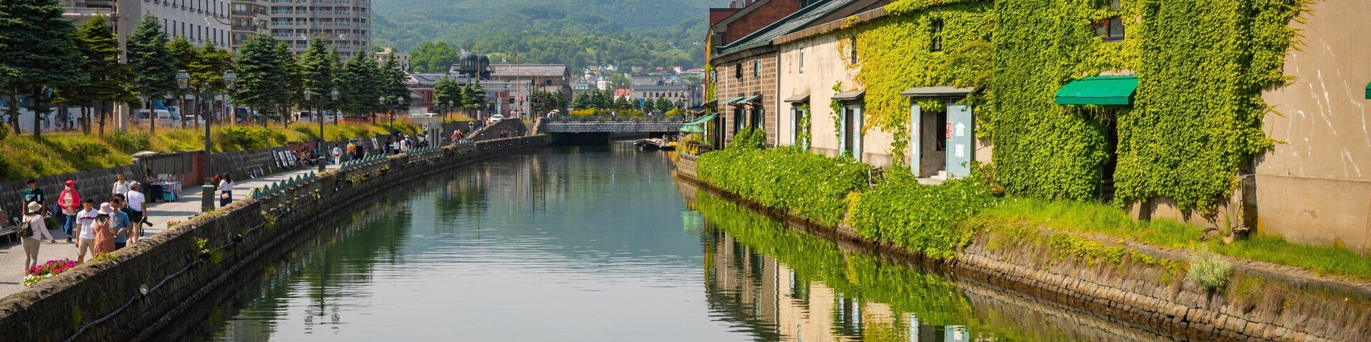 Um canal tranquilo com edifícios em ambos os lados, incluindo uma casa coberta de hera e um edifício moderno com cúpula.