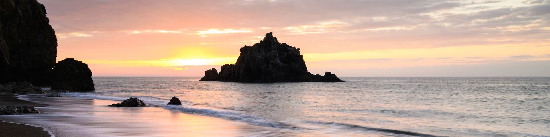 A beach with waves, a sunset, and rocky formations.