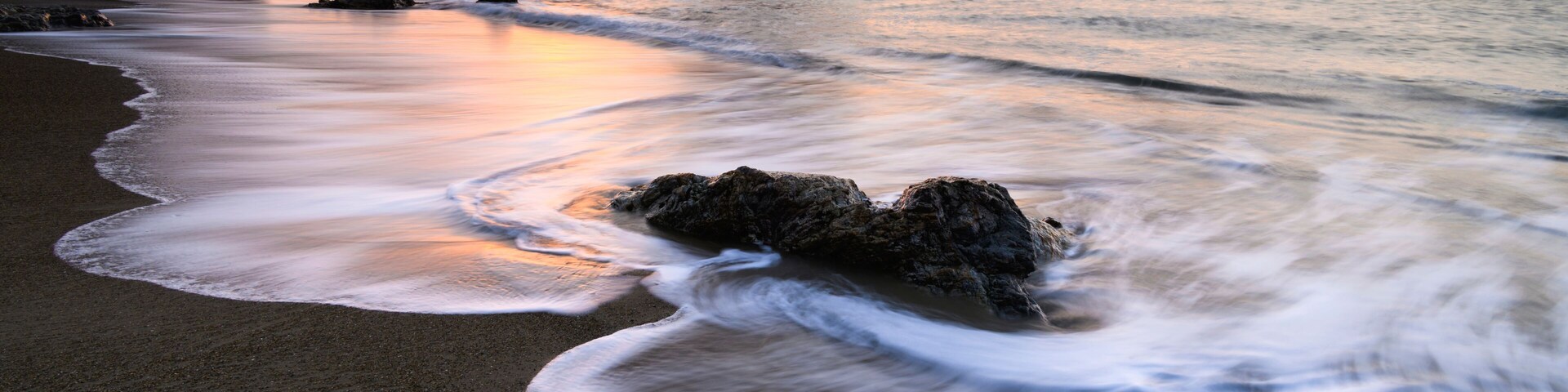 A beach with waves, a sunset, and rocky formations.