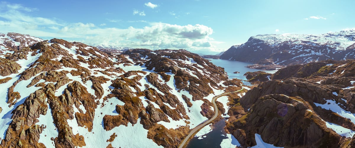 A rugged mountainous landscape with snow patches and a winding road.