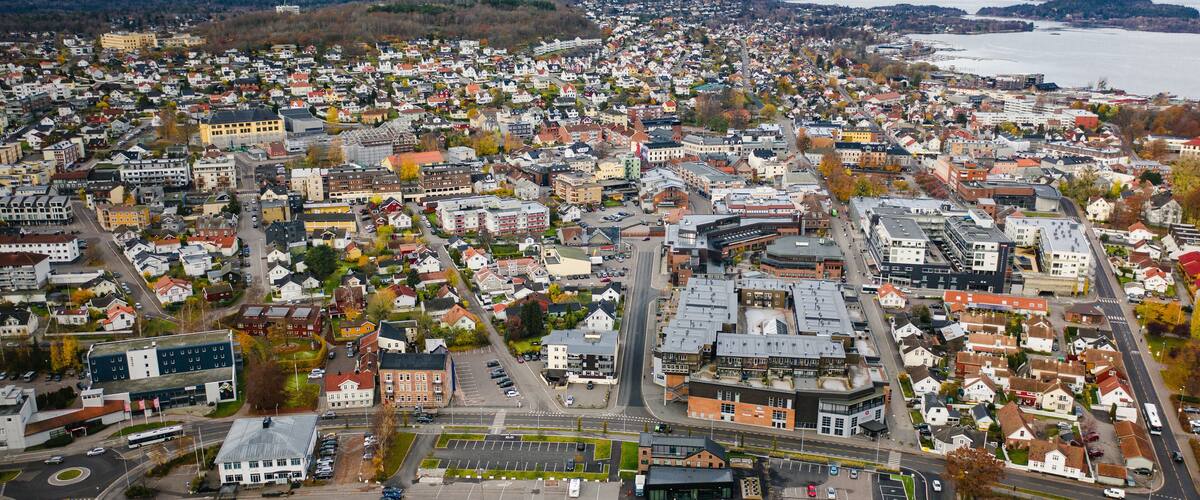 An aerial view of a densely populated town with a mix of residential and commercial buildings, a large body of water in the background, and a prominent round building in the center.