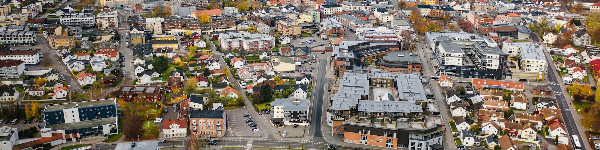 An aerial view of a densely populated town with a mix of residential and commercial buildings, a large body of water in the background, and a prominent round building in the center.