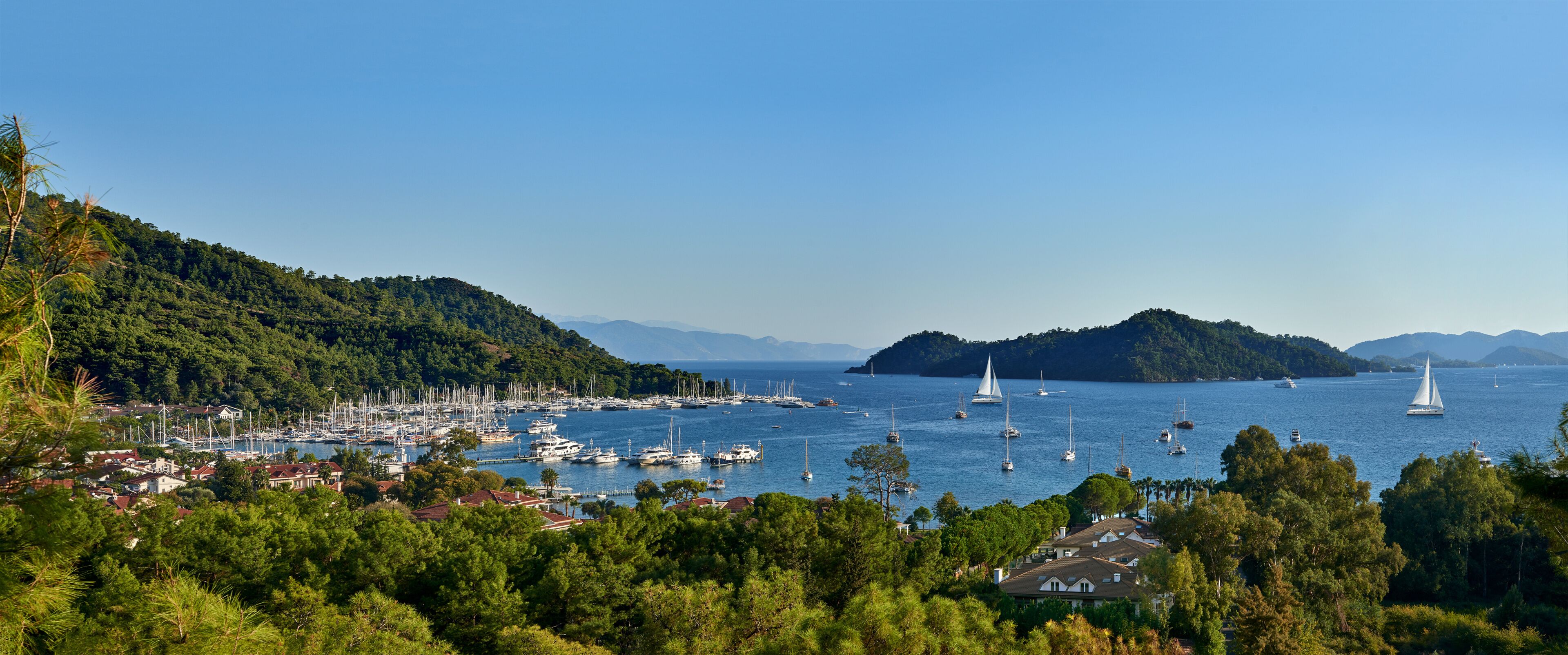 A coastal town with a marina, sailboats, and lush green hills.