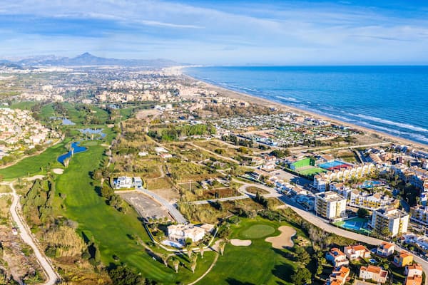 Una ciudad costera con un campo de golf, zonas residenciales y montañas al fondo.