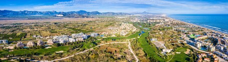 Eine Küstenstadt mit Golfplatz, Wohngebieten und Bergen im Hintergrund.