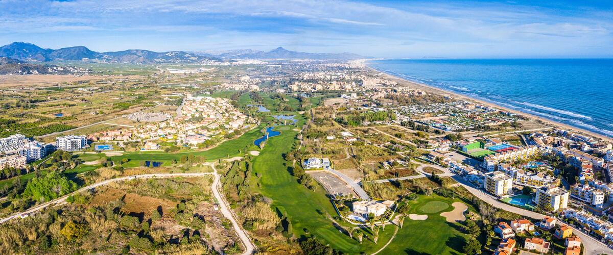 A coastal city with a golf course, residential areas, and mountains in the background.