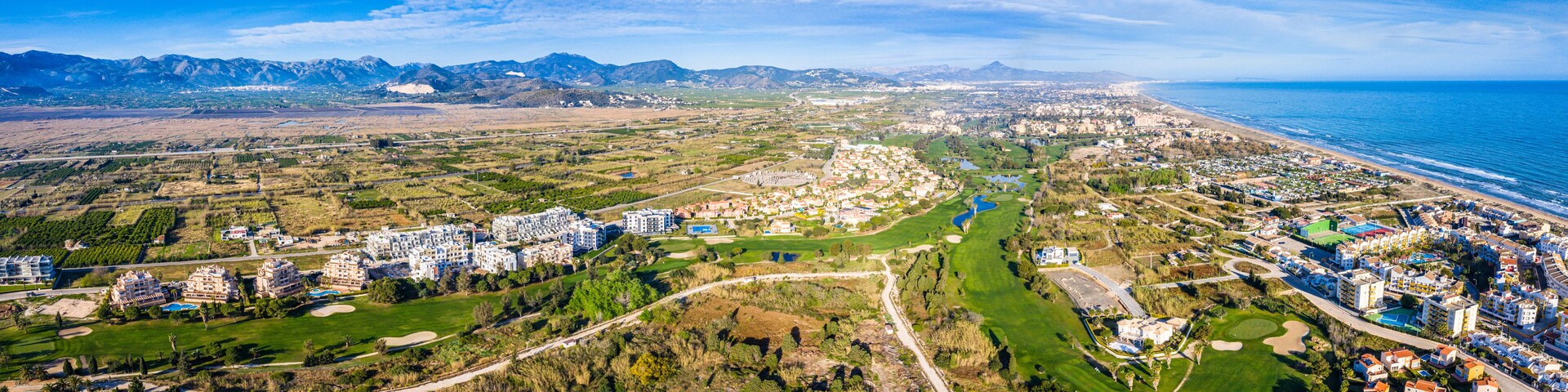 A coastal city with a golf course, residential areas, and mountains in the background.