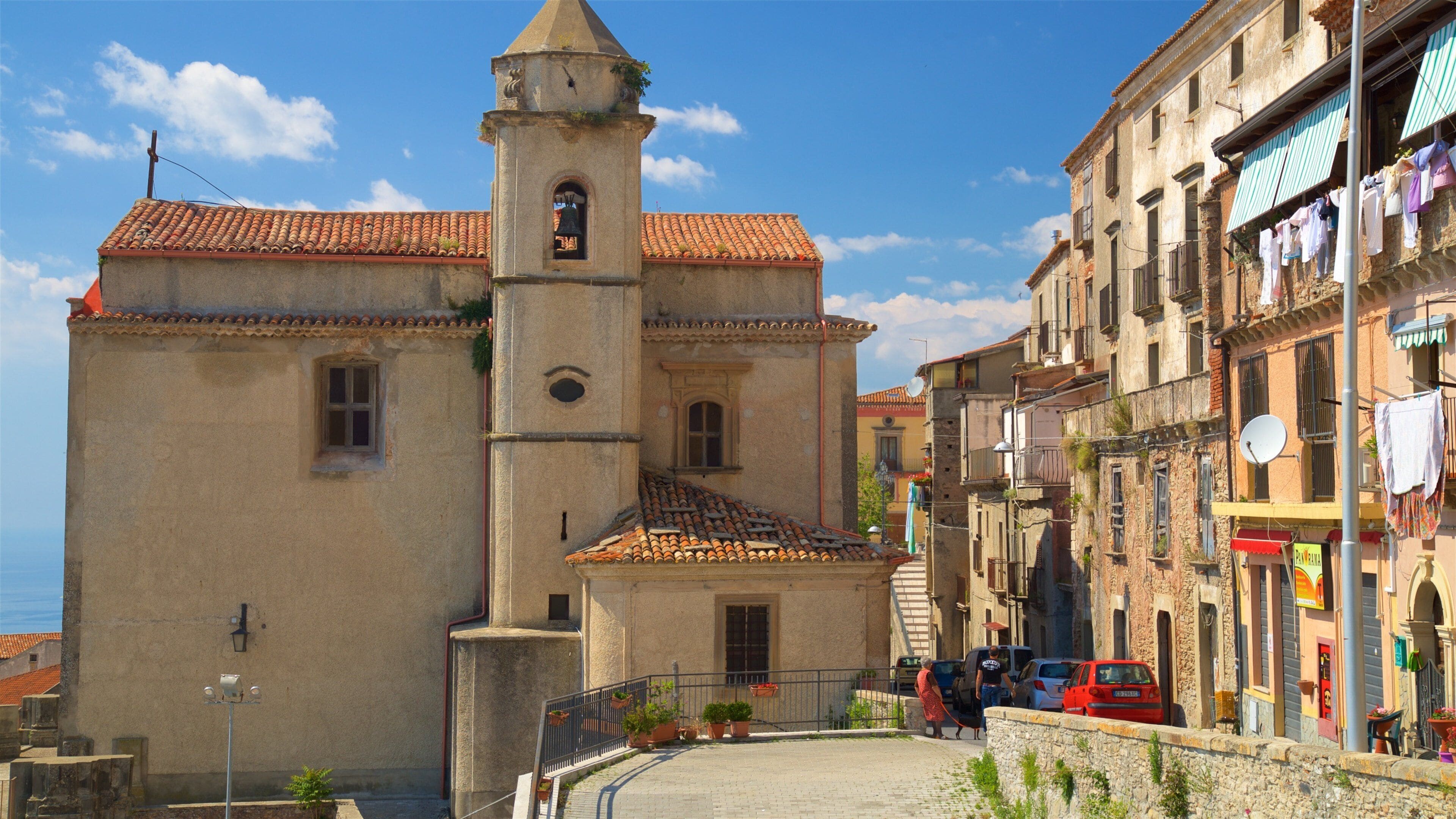 A historic church with a bell tower, terracotta roof tiles, and a cobblestone street.