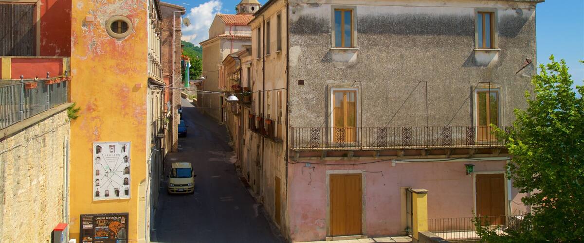 A narrow street flanked by colorful buildings, a parked car, and a clear blue sky.