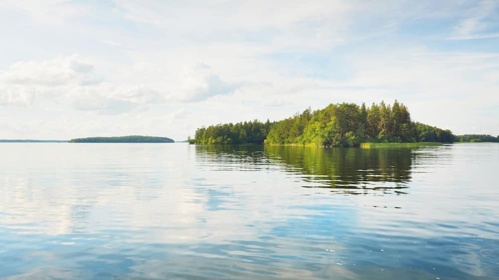 Rocky lakeshore and forest on a sunny summer day. Green trees, plants. Bålsta, Mälaren lake, Sweden. Idyllic landscape. Reflections on water. Nature, ecology, environment, ecotourism, hiking