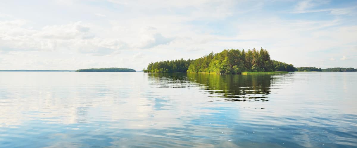 Rocky lakeshore and forest on a sunny summer day. Green trees, plants. Bålsta, Mälaren lake, Sweden. Idyllic landscape. Reflections on water. Nature, ecology, environment, ecotourism, hiking