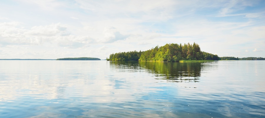 Rocky lakeshore and forest on a sunny summer day. Green trees, plants. Bålsta, Mälaren lake, Sweden. Idyllic landscape. Reflections on water. Nature, ecology, environment, ecotourism, hiking