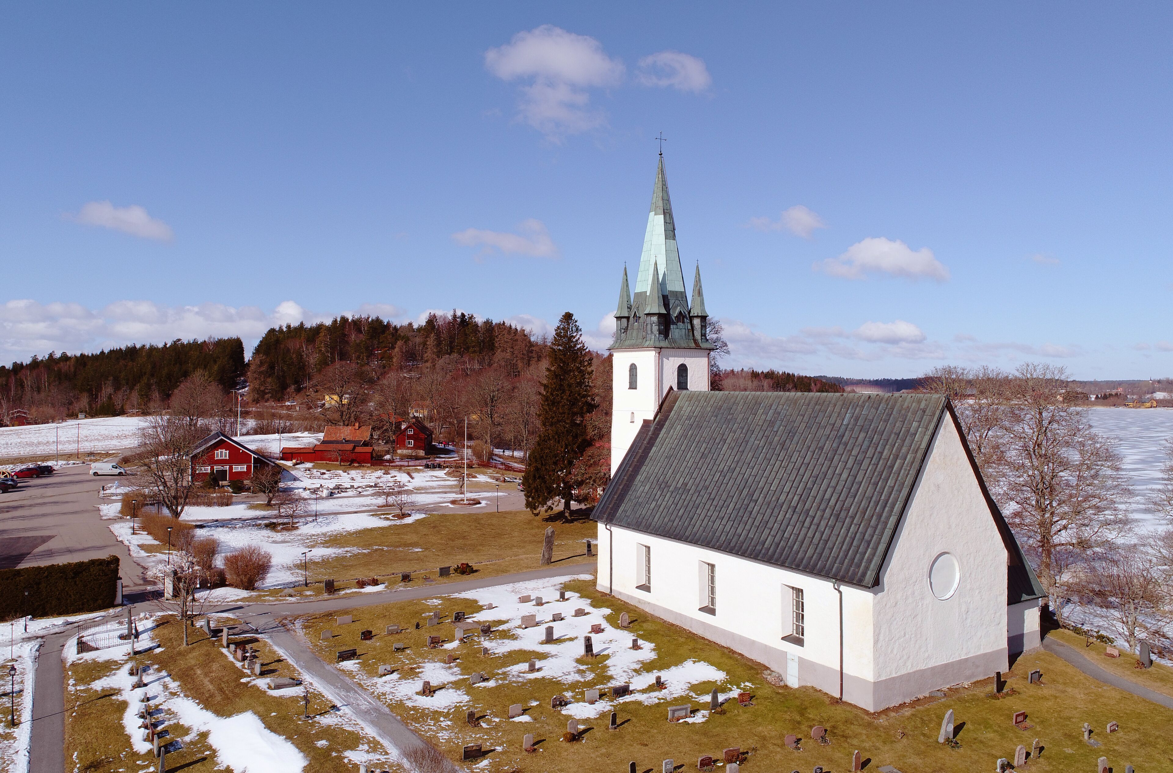 A church with a tall steeple, a cemetery, and a red barn in a rural setting.