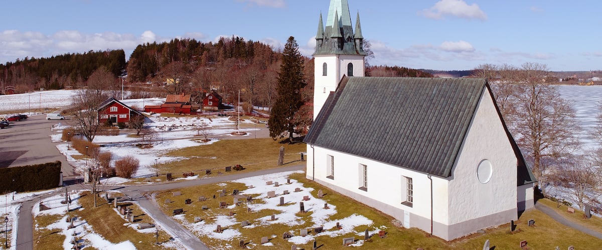 A church with a tall steeple, a cemetery, and a red barn in a rural setting.