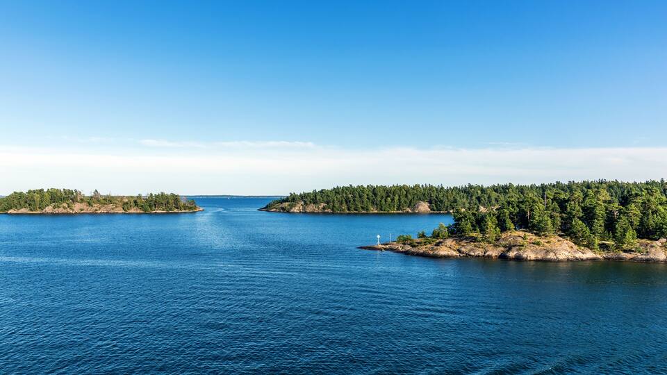 A large body of water with two small islands, one with a wind turbine and the other with dense forest.