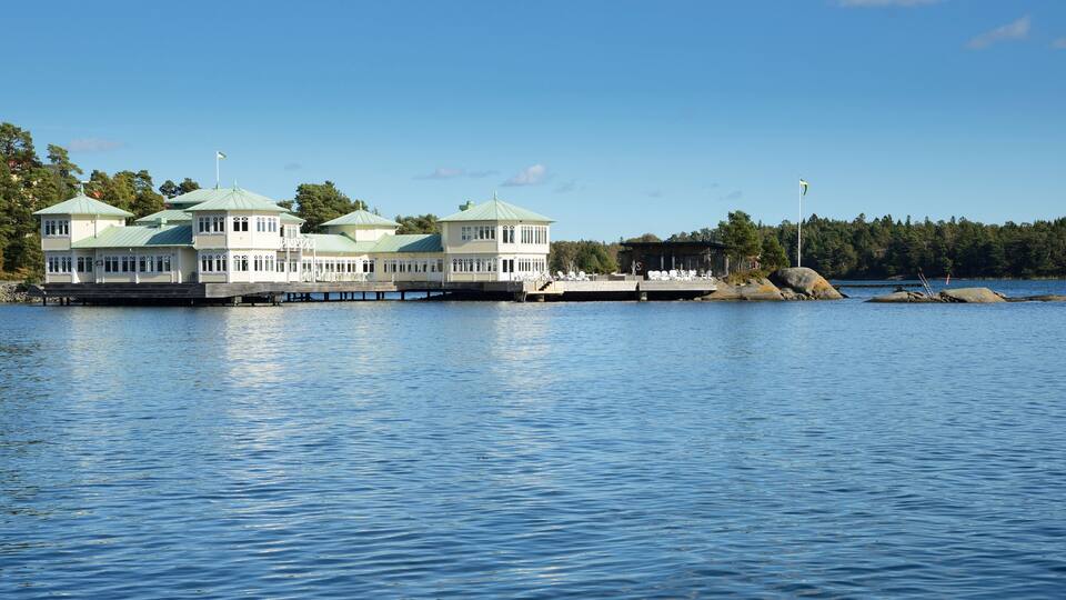A waterfront property with multiple green-roofed buildings, a dock, and a forested shoreline.