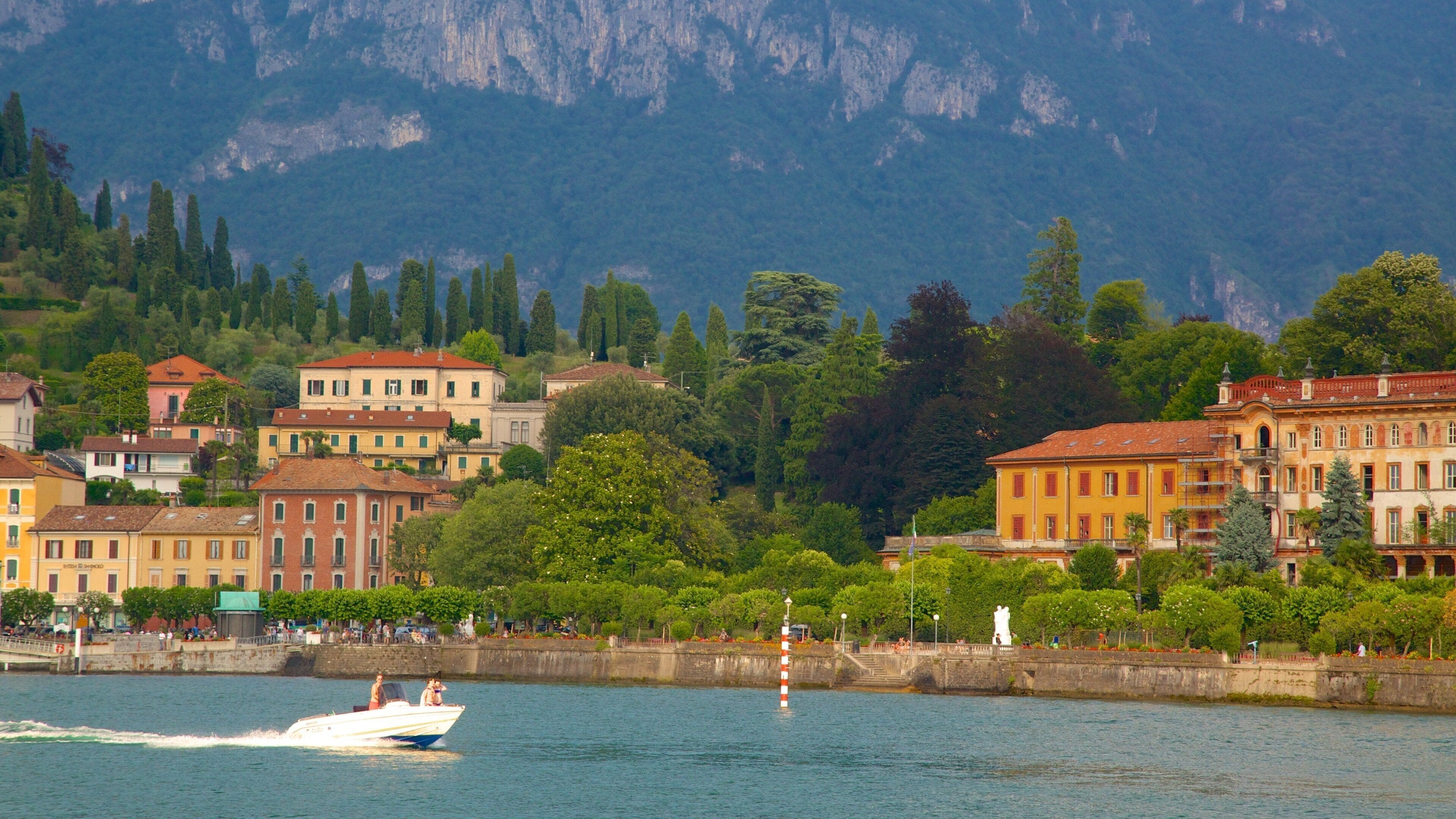 Un lago con una barca, edifici e montagne sullo sfondo.