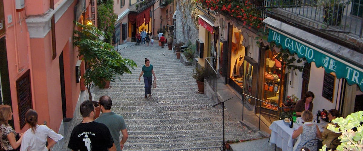 A cobblestone street in a European town with shops and people walking.