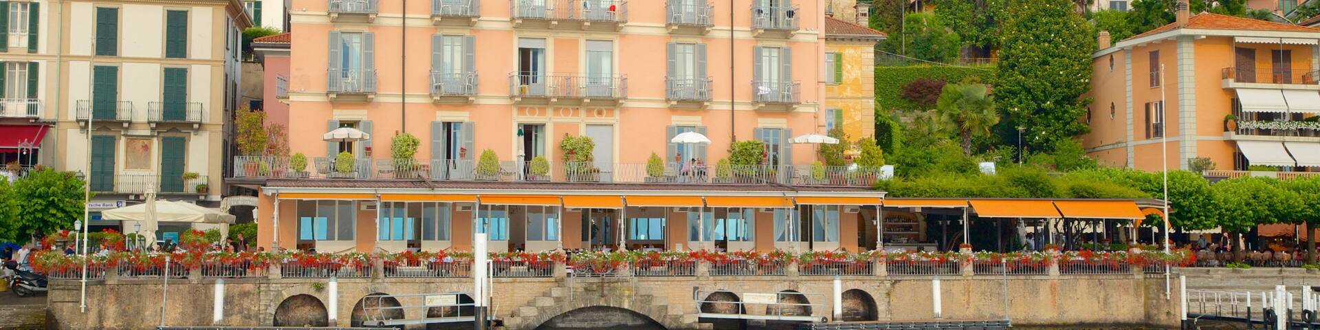 A waterfront hotel with balconies overlooking a canal, surrounded by lush greenery and mountains.