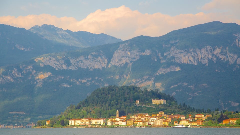 A lakeside town with historic buildings, a prominent church tower, and mountains in the background.