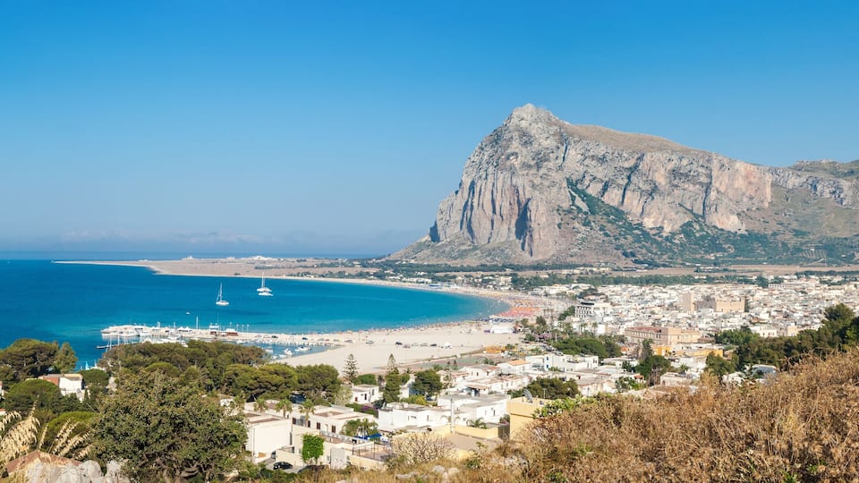 A coastal town with a beach, marina, and mountainous backdrop.