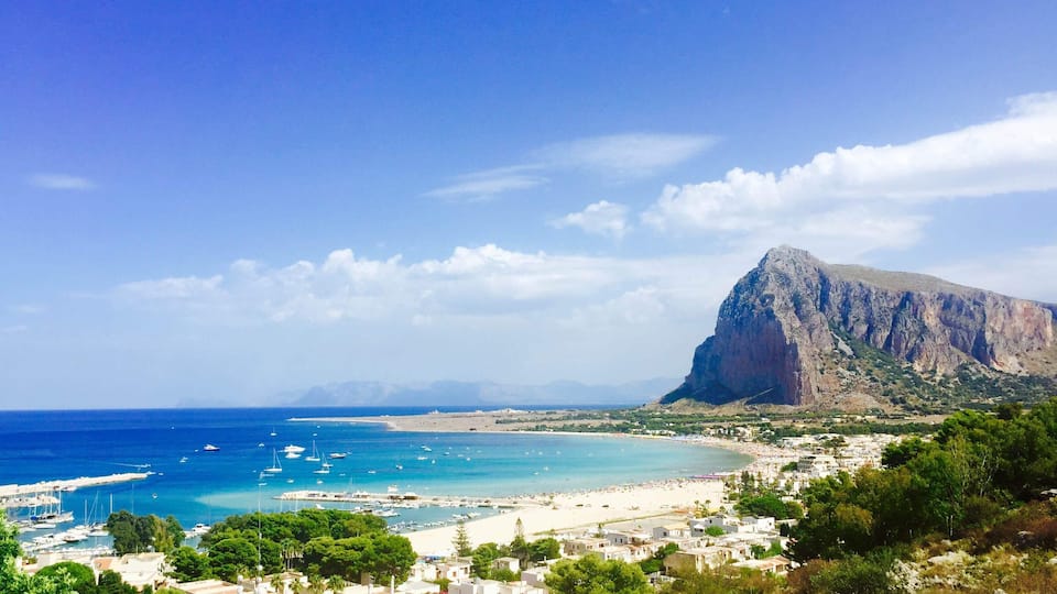 A coastal town with a prominent mountain, a beach, and a marina.