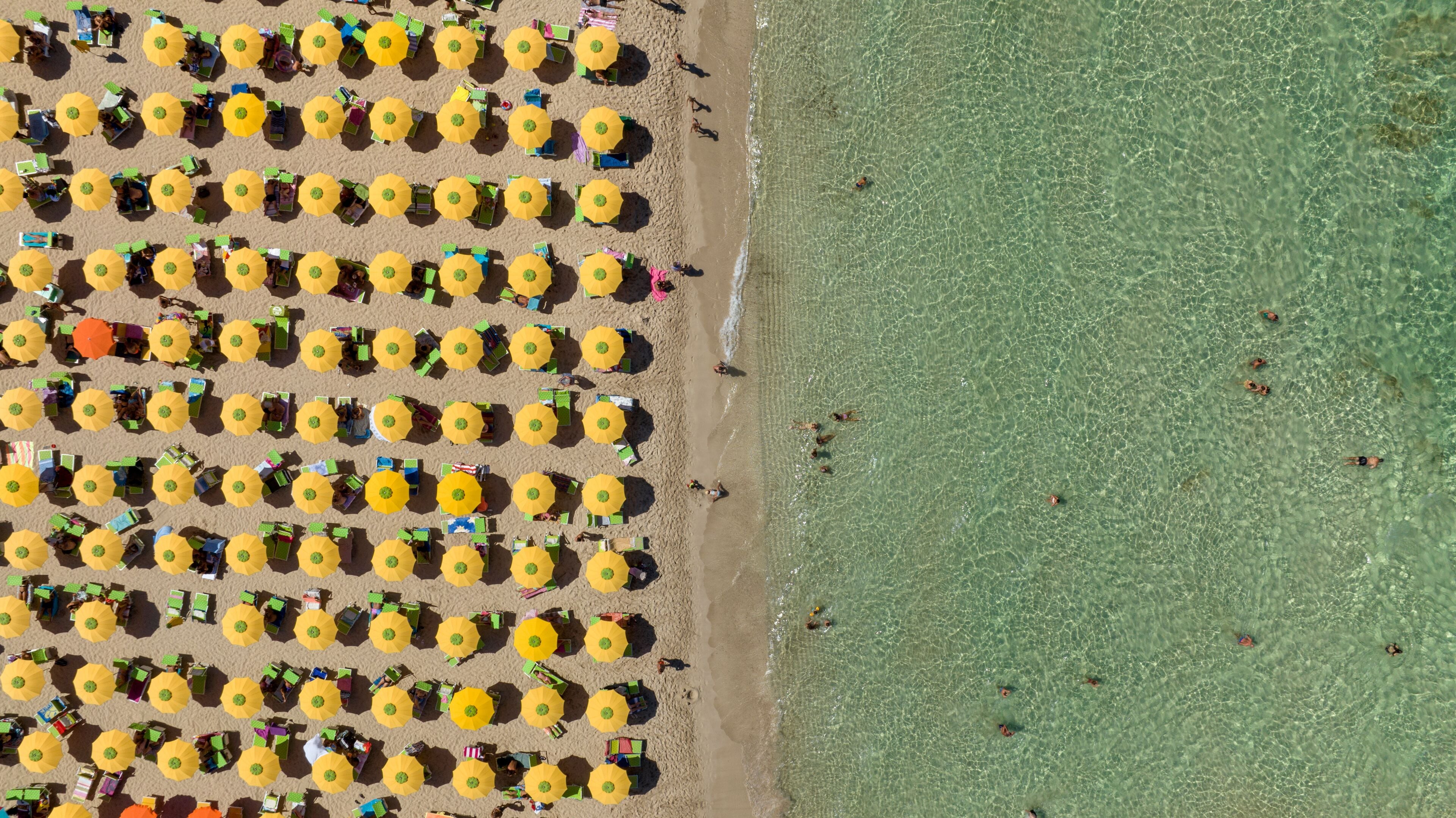 Perpendicular aerial view of the beach at San Vito Lo Capo, located in the province of Trapani, Sicily, Italy. There are many beach resorts and parasols with tourists on holiday.