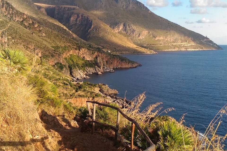 A coastal path with a wooden railing, rocky terrain, and a mountain in the background.