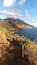 A coastal path with a wooden railing, rocky terrain, and a mountain in the background.