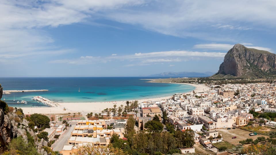 A coastal town with a beach, rocky cliffs, and a mountain in the background.