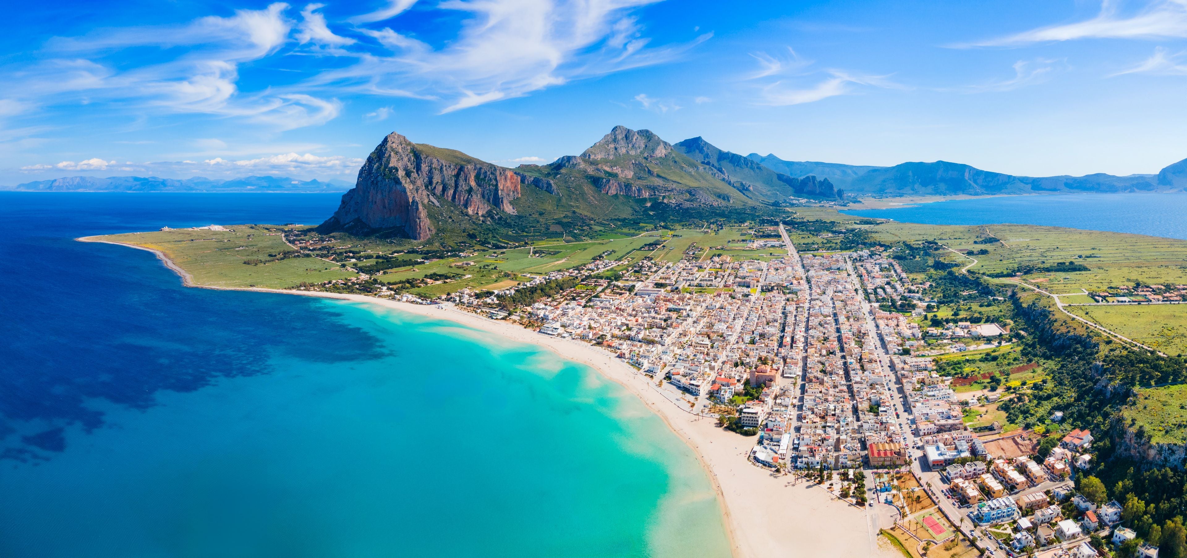 A coastal town with a beach, mountains, and a clear sky.