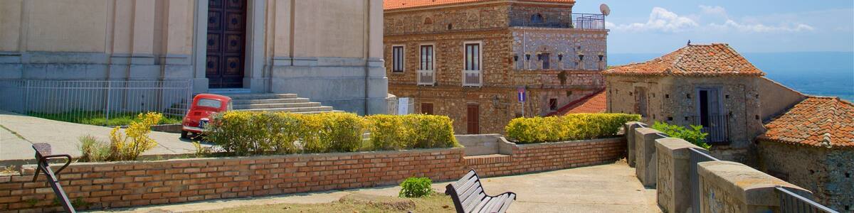 A historic building with a red-tiled roof, a stone building with a balcony, and a bench in a landscaped area.
