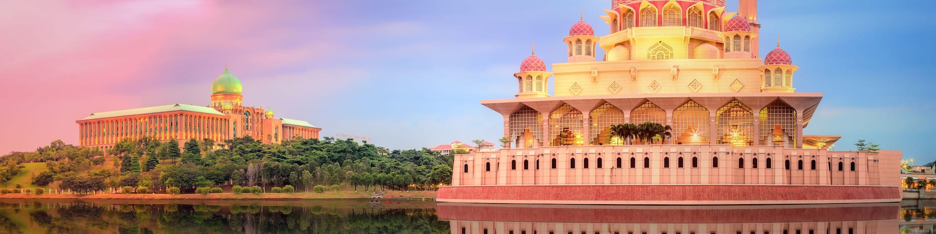 A large mosque with a golden dome and minarets, reflecting in a calm body of water, with a smaller building in the background.