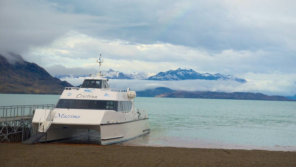 A boat named 'Cristina' docked at a pier with a mountainous landscape in the background.
