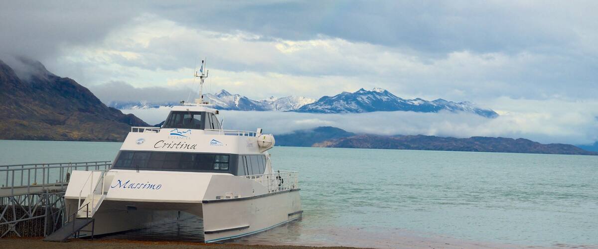 A boat named 'Cristina' docked at a pier with a mountainous landscape in the background.
