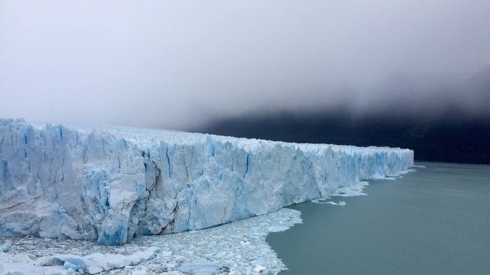 A glacier with a large ice wall and floating ice chunks in a body of water.