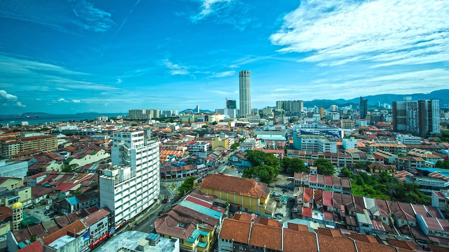 A coastal cityscape with a prominent tall building, dense urban architecture, and a clear blue sky.